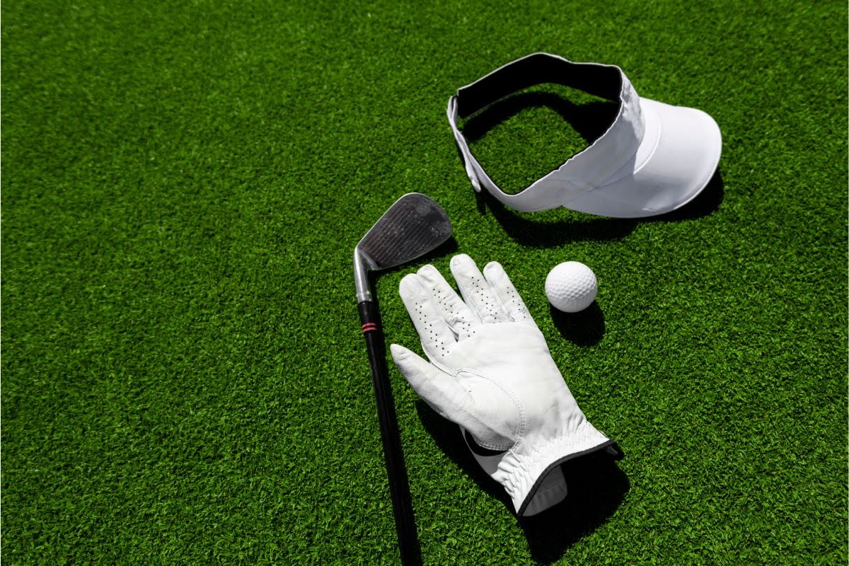 Golf ball, club, glove, and visor lying on grass.